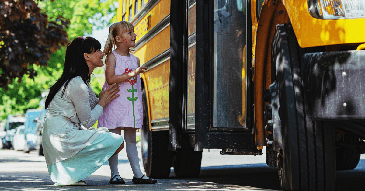 A mother reassures her daughter at a school bus pickup.