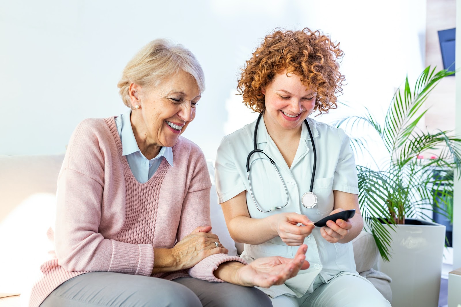 A caregiver sits with a senior smiling while carrying out medical checks